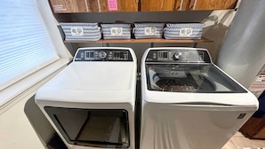 Two front-loading washing machines in a room with a window and a shelf above containing patterned baskets.
