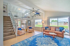 A spacious living room with a staircase, a ceiling fan, a large window, and a blue patterned rug. - Sanders Island View Home Steps to Lake Texoma (Kingston)