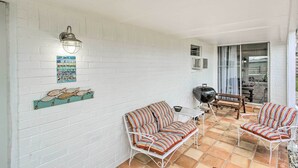A patio with white brick walls, a striped sofa, a metal table, and a grill.