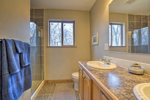 Ein Badezimmer mit Glasdusche, Toilette, Waschbecken mit Spiegel und Fenster.