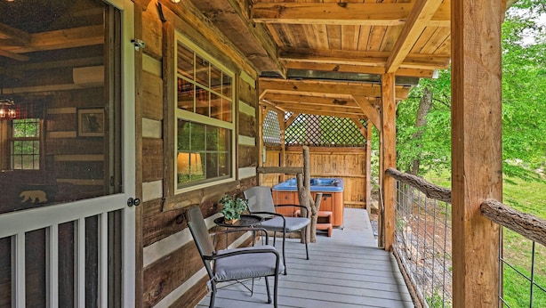 A wooden deck with a table and chairs, a hot tub, and a view of the surrounding greenery.