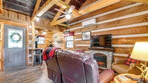 A log cabin interior with a fireplace, leather sofa, and a dining area.