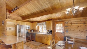 A log cabin kitchen with wooden cabinets, stainless steel appliances, and a dining area with a table set for four. - Pine Mountain Club Cabin Rental w/ Pool Access! (Pine Mountain Club)