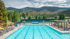 A swimming pool with lounge chairs and umbrellas, surrounded by a fence and trees, with mountains in the background. - Pine Mountain Club Cabin Rental w/ Pool Access! (Pine Mountain Club)