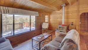 A cozy cabin with a wooden interior, a fireplace, a sofa, and a large window offering a view of the outdoors. - Pine Mountain Club Cabin Rental w/ Pool Access! (Pine Mountain Club)