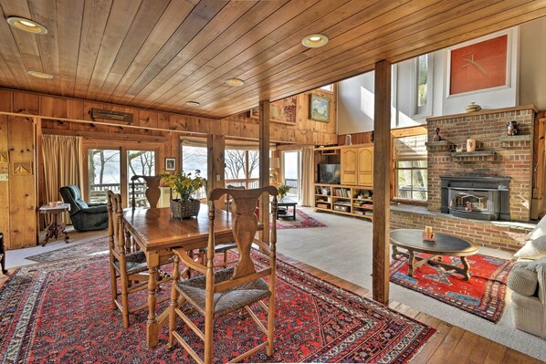 A spacious living room with a wooden ceiling, a fireplace, and a large window overlooking a snowy landscape.