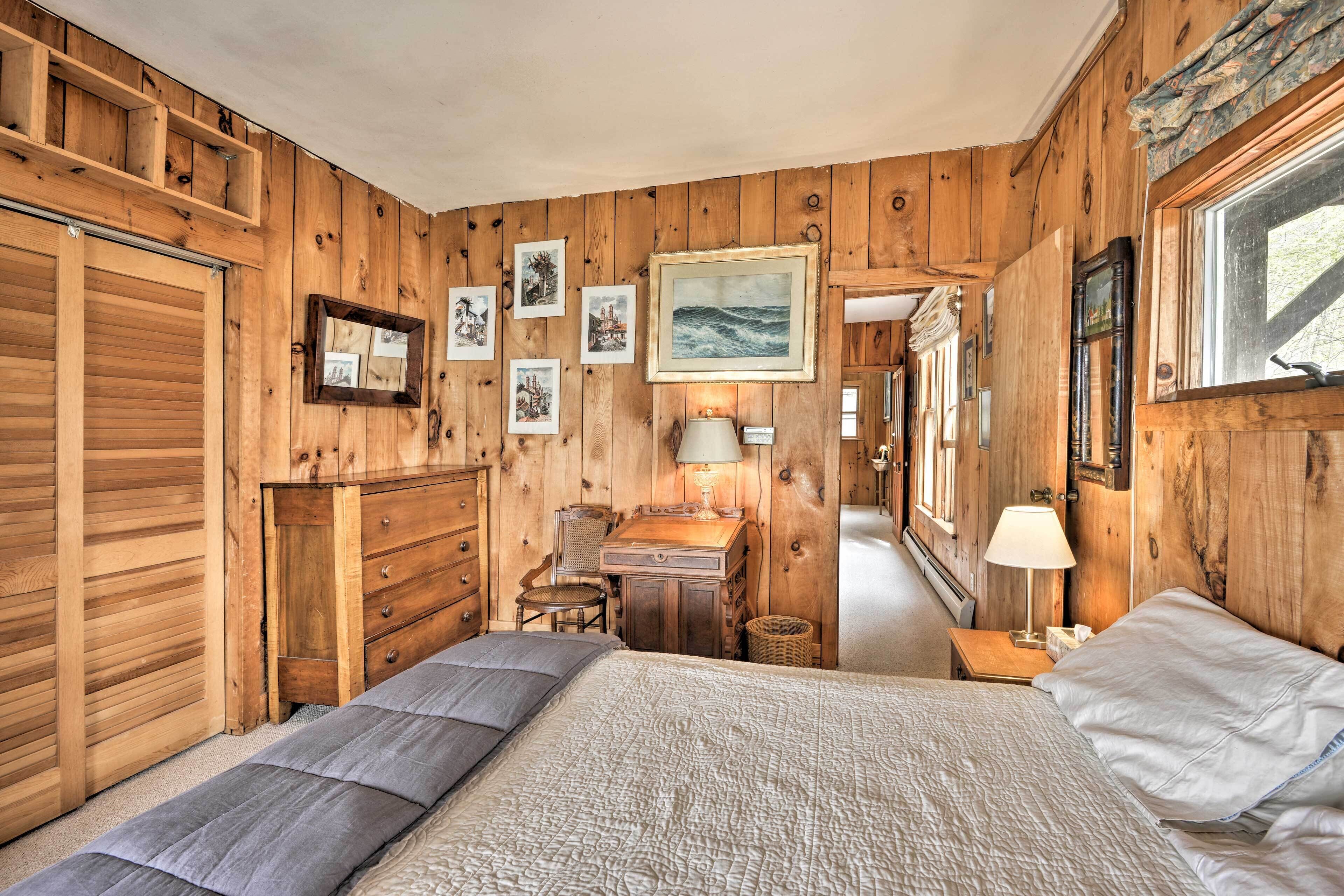 Ein Zimmer mit Holzboden, einem Bett, einem Schreibtisch und einem Stuhl. An der Wand hängen gerahmte Bilder.