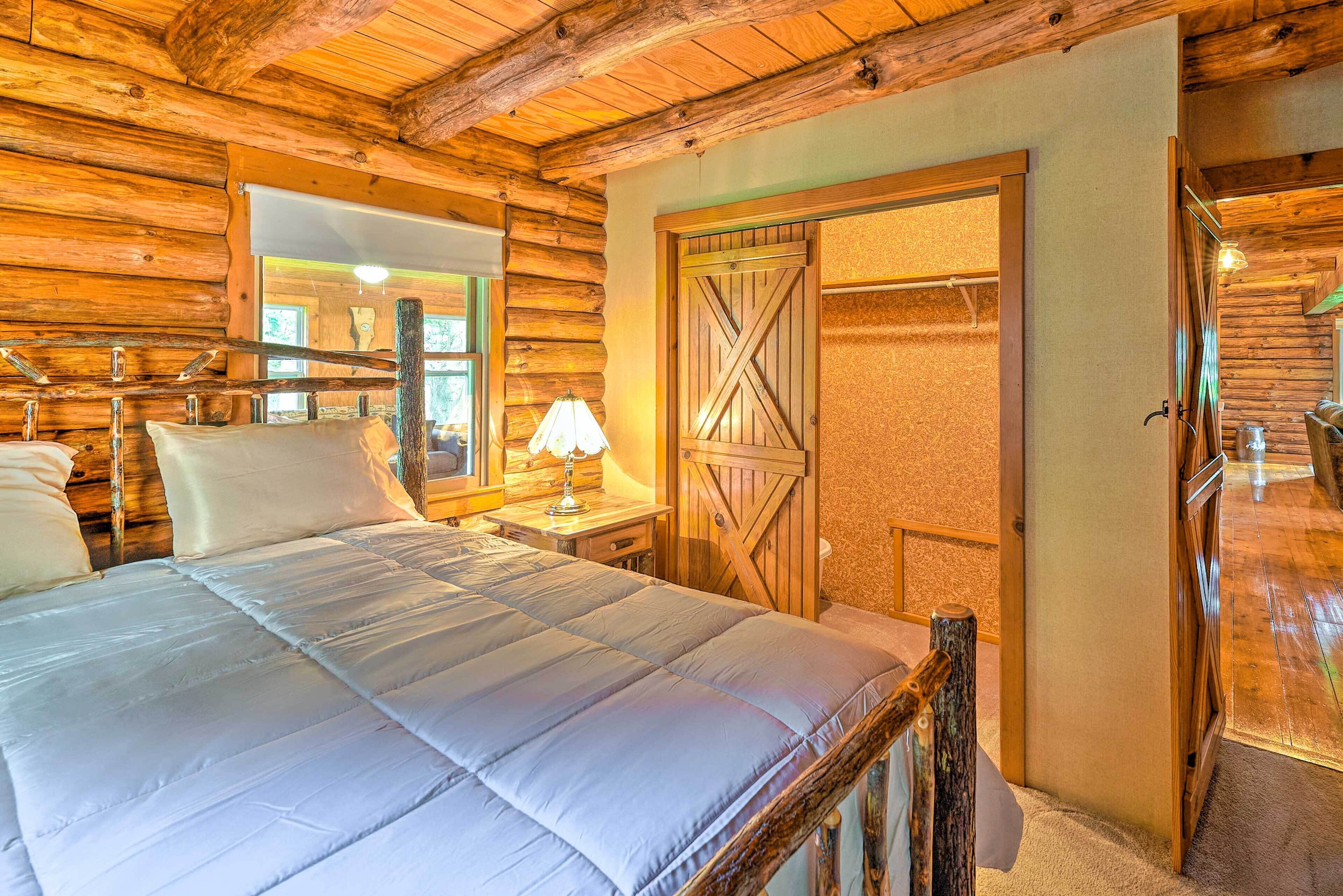 A log cabin bedroom with a large bed, wooden walls, a wooden door, and a window with a view.