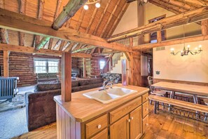 A rustic cabin interior with a wooden dining table, a kitchen area with a sink, and a cozy seating area with a fireplace. - Rustic Zanesville Getaway w/ Expansive Yard! (Zanesville)