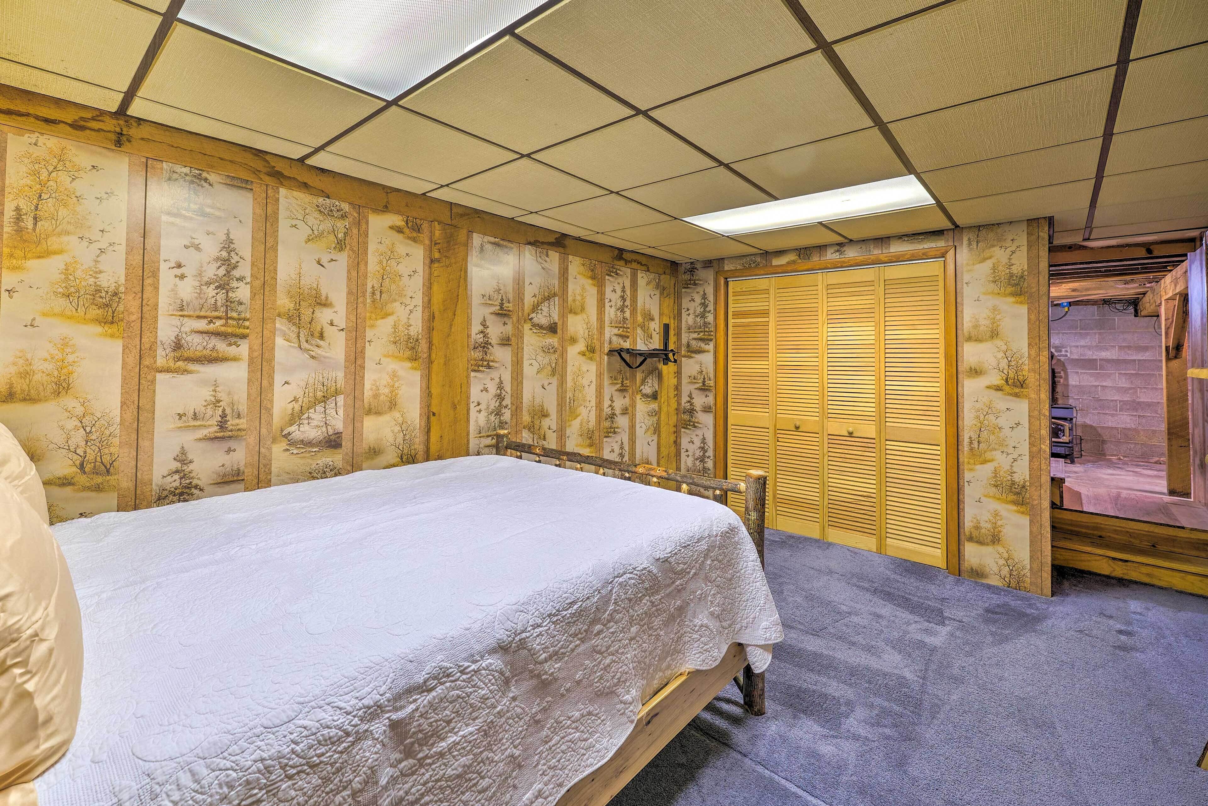 Una habitación con una cama, cabecera de madera, un mural temático de naturaleza en la pared, un armario de madera y suelo alfombrado.