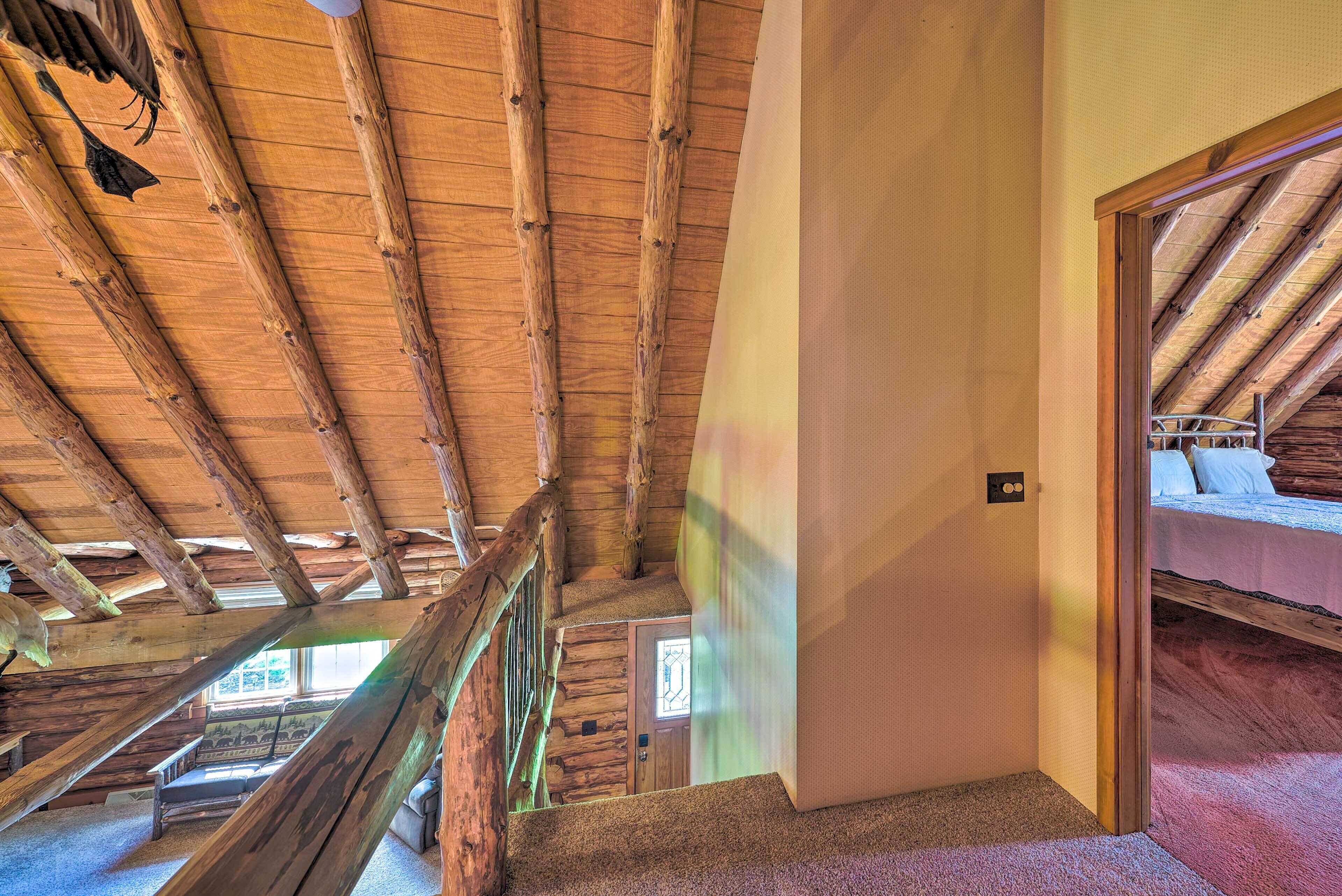 Un escalier en bois mène à une chambre située en mezzanine, avec un plafond en pente et une vue sur l’extérieur.