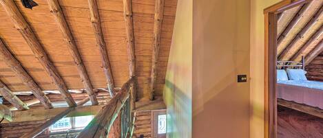 Un escalier en bois mène à une chambre située en mezzanine, avec un plafond en pente et une vue sur l’extérieur.