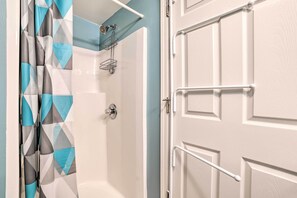 A bathroom with a shower, a towel rack, and a door with a white handle. - Pool + Hot Tub Access! Portage Lake Condo w/ Deck (Onekama)