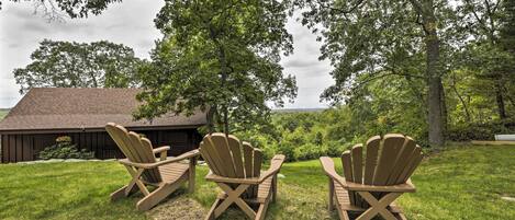 Three Adirondack chairs in a grassy area with a wooden building in the background.
