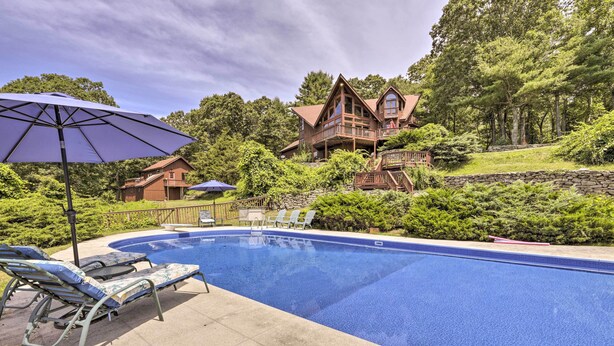 Une piscine entourée d’une terrasse en bois et d’une végétation luxuriante, avec des chaises longues et des parasols à proximité.