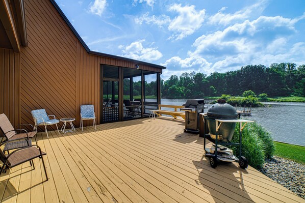 A wooden deck with outdoor furniture, a grill, and a view of a lake. - Cozy Fireside Retreat: Private Plymouth Lake Home! (Plymouth)