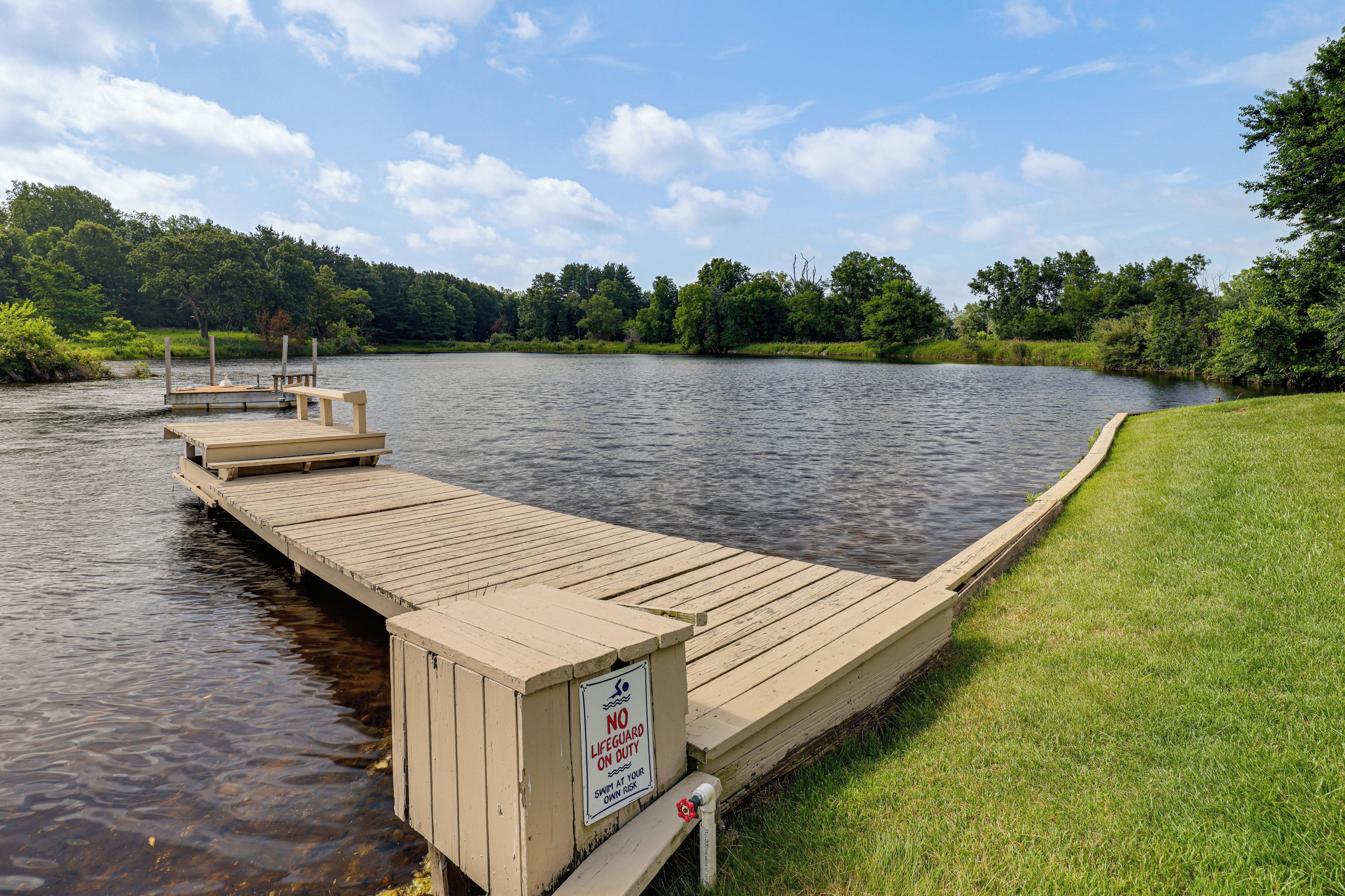 A wooden dock extending into a calm lake, surrounded by lush greenery and a clear sky.