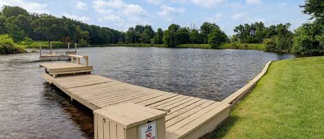 A wooden dock extending into a calm lake, surrounded by lush greenery and a clear sky.