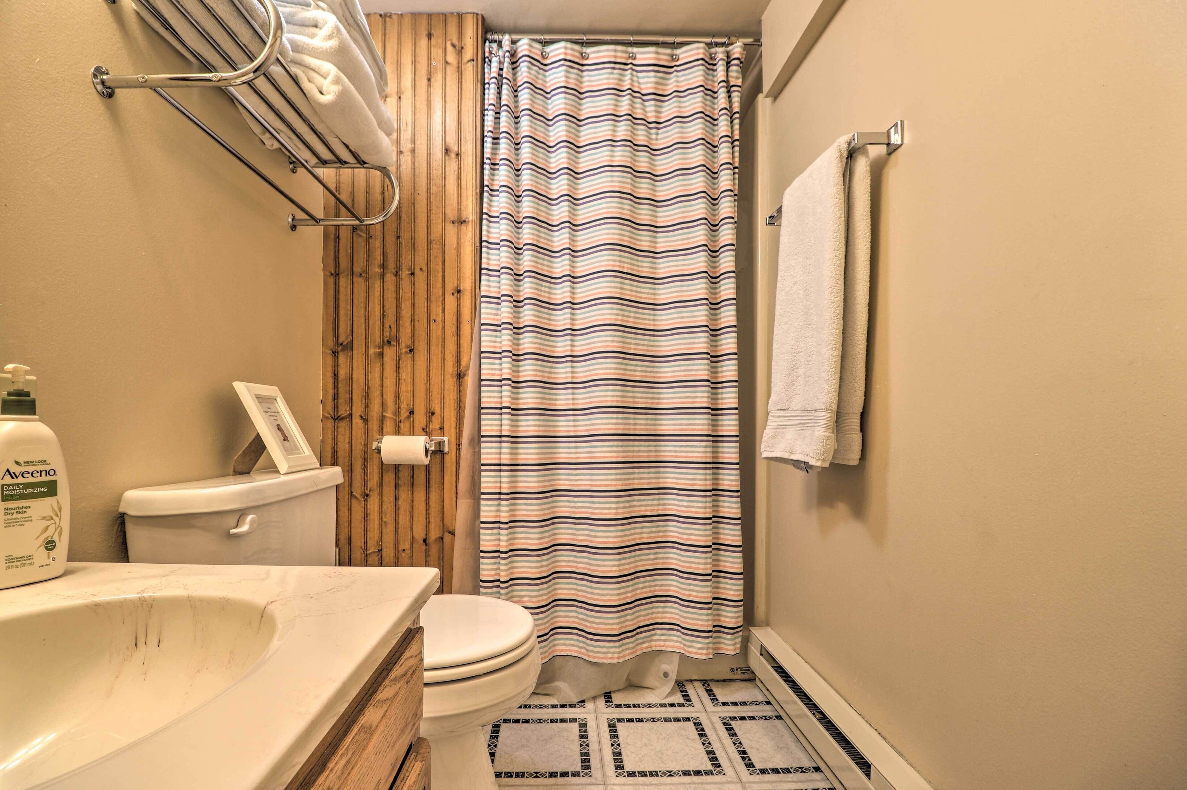 A bathroom with a wooden panel wall, a striped shower curtain, a toilet, a sink with a soap dispenser, and a towel rack.