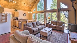 A spacious living area with a large wooden ceiling, a cozy fireplace, and a kitchen with wooden cabinets and a sink. - Riverfront Hungry Horse House With Large Deck! (Hungry Horse)