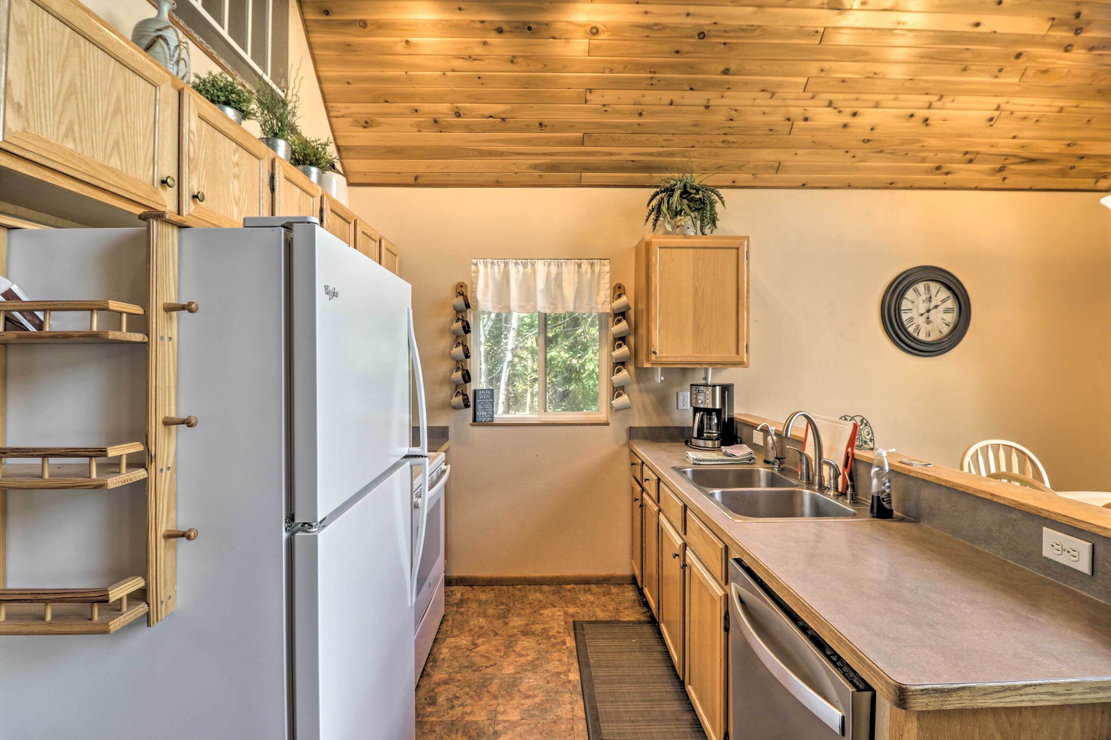 A compact kitchen with wooden cabinets, a built-in refrigerator, a sink, and a window with curtains.