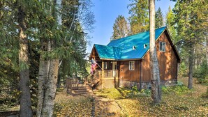 A wooden cabin with a green roof surrounded by trees. - Riverfront Hungry Horse House With Large Deck! (Hungry Horse)