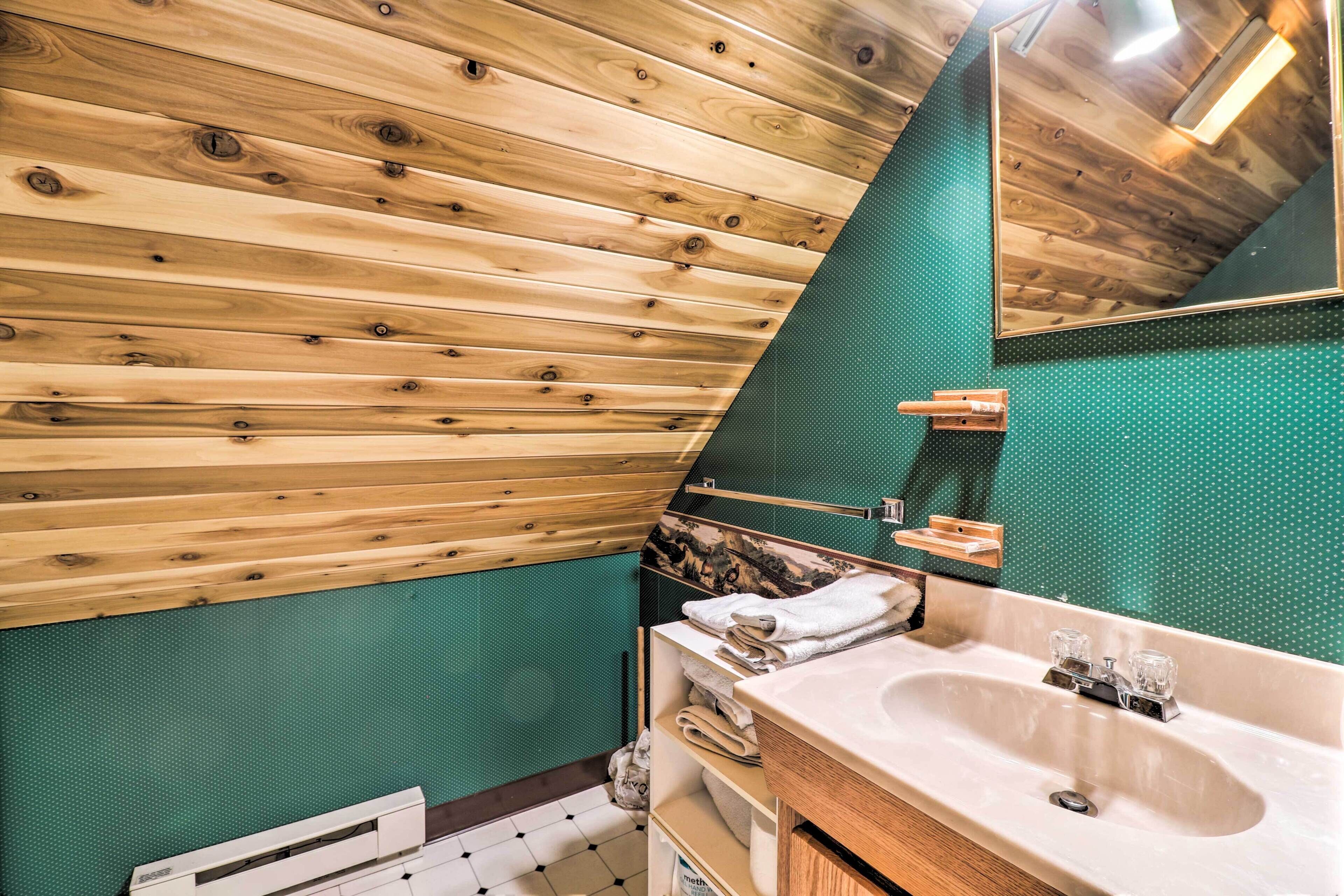 A bathroom with wooden slats on the ceiling, a green textured wall, and a sink with a mirror.