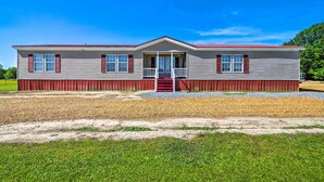 A two-story house with a front porch, a red door, and a gravel driveway.