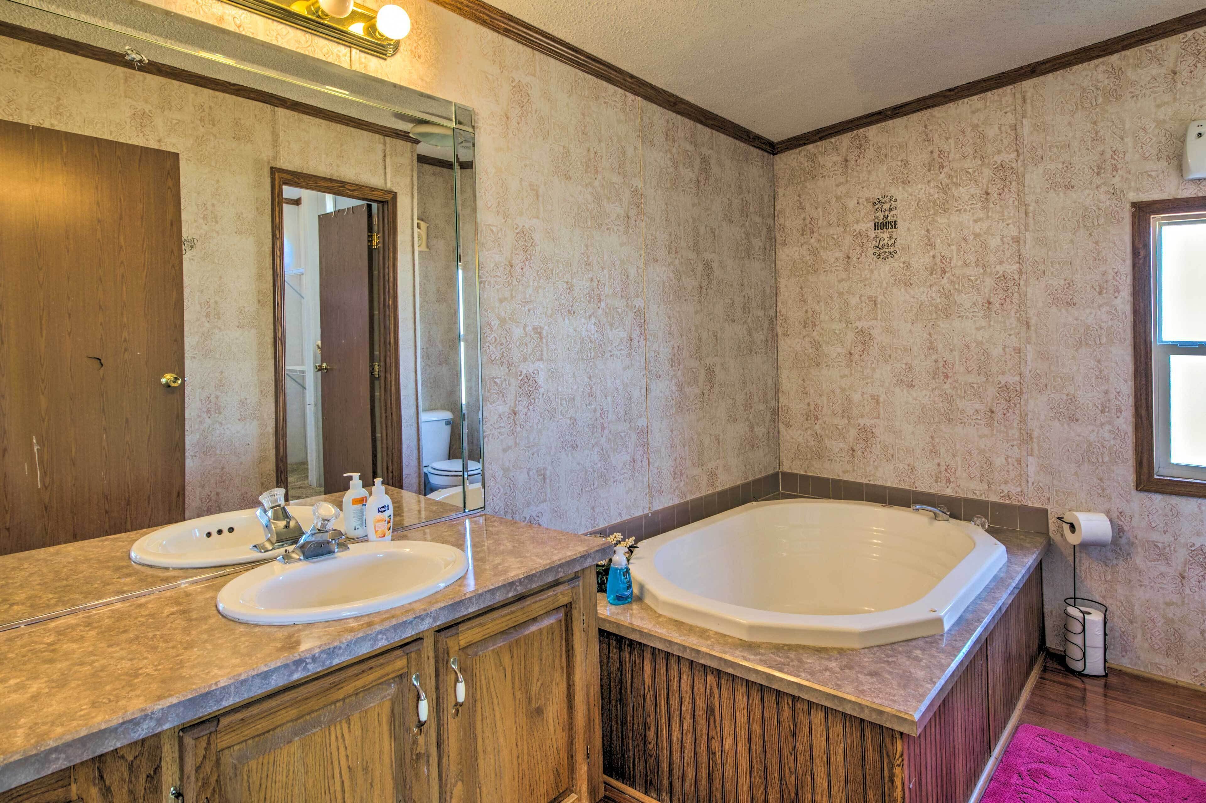 A bathroom with two sinks, a large bathtub, wooden cabinets, a mirror, and a window.