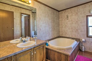 A bathroom with two sinks, a large bathtub, wooden cabinets, a mirror, and a window.