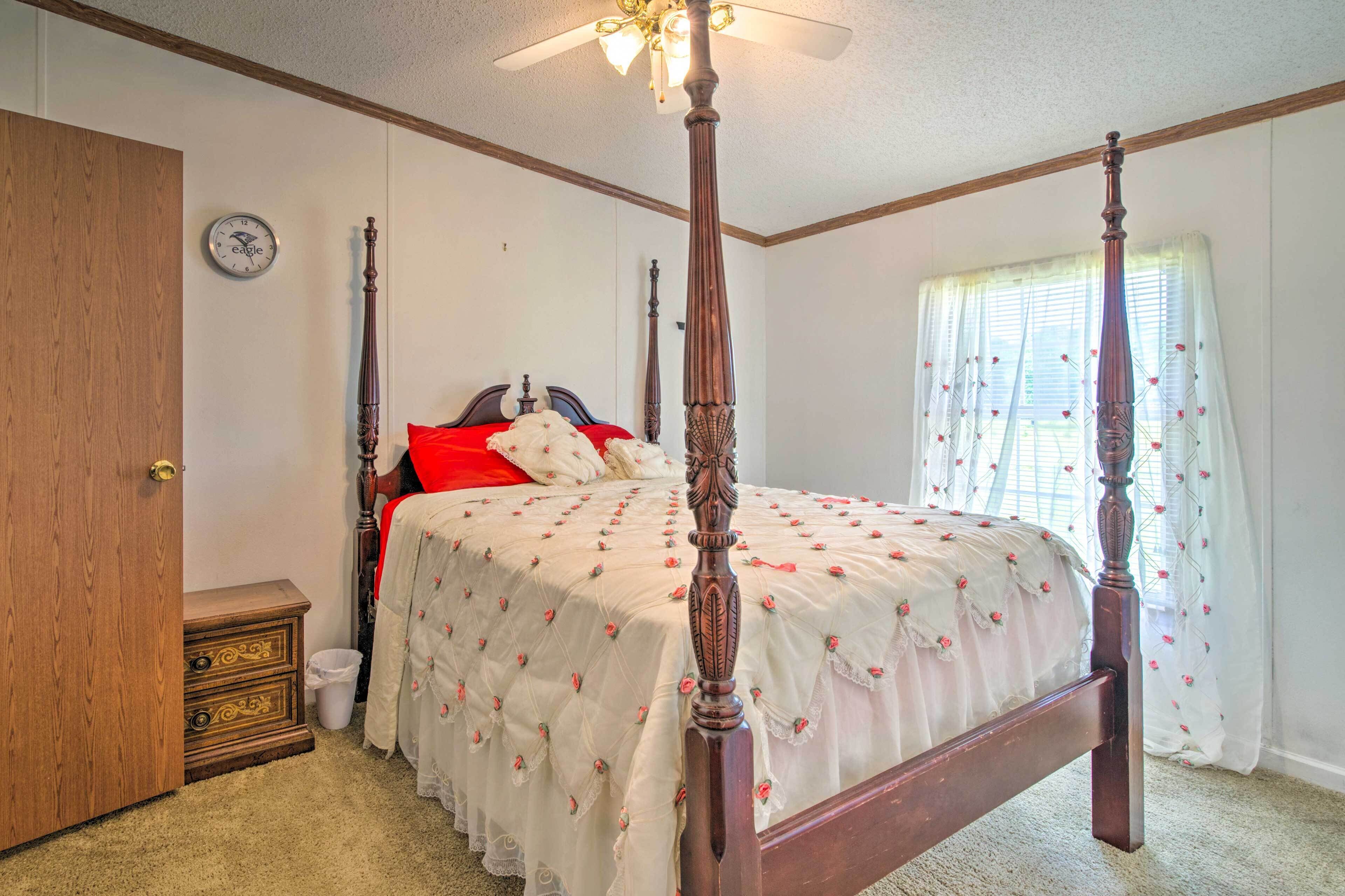 Quarto com cama de dossel, mesa de cabeceira de madeira, relógio na parede e janela com cortinas leves.
