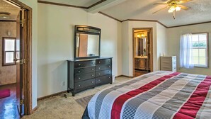 A bedroom with a large bed, a dresser, a ceiling fan, and a window with curtains.