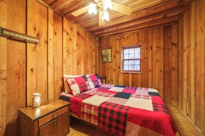 A wooden cabin bedroom with a bed, a nightstand, a window, and a ceiling fan. - Rustic Cabin w/ Mountain Views! Elevation 4,400 (Maggie Valley)