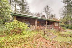 A rustic cabin with a green roof and wooden exterior, surrounded by dense foliage and trees. - Rustic Cabin w/ Mountain Views! Elevation 4,400 (Maggie Valley)