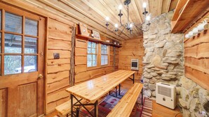 A wooden cabin interior with a stone wall, wooden benches, a table, and a ceiling light fixture. - Rustic Maggie Valley Cabin w/ Mountain Views! (Maggie Valley)