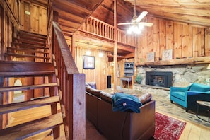 A wooden interior with a staircase, a fireplace, a sofa, and a ceiling fan. - Rustic Cabin w/ Mountain Views! Elevation 4,400 (Maggie Valley)