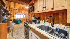 A rustic kitchen with wooden cabinets, a granite countertop, a sink, a stove, and a coffee maker. - Rustic Maggie Valley Cabin w/ Mountain Views! (Maggie Valley)