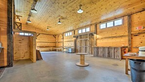 A spacious barn-style interior with wooden walls and a concrete floor, featuring a central table, a fire extinguisher, and an exit sign.