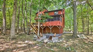 Eine Hütte im Wald mit einer Holzdielen-Terrasse und einer Treppe, die zu einem Balkon führt.