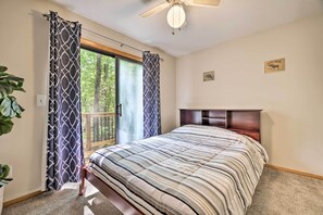 Een slaapkamer met een bed, een plafondventilator, een raam met gordijnen en een houten hoofdeinde.