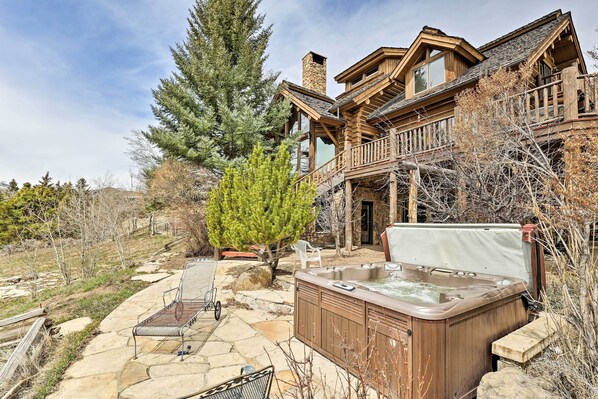 Une grande maison en bois dotée d’un jacuzzi, d’une terrasse en pierre et d’un grand arbre.