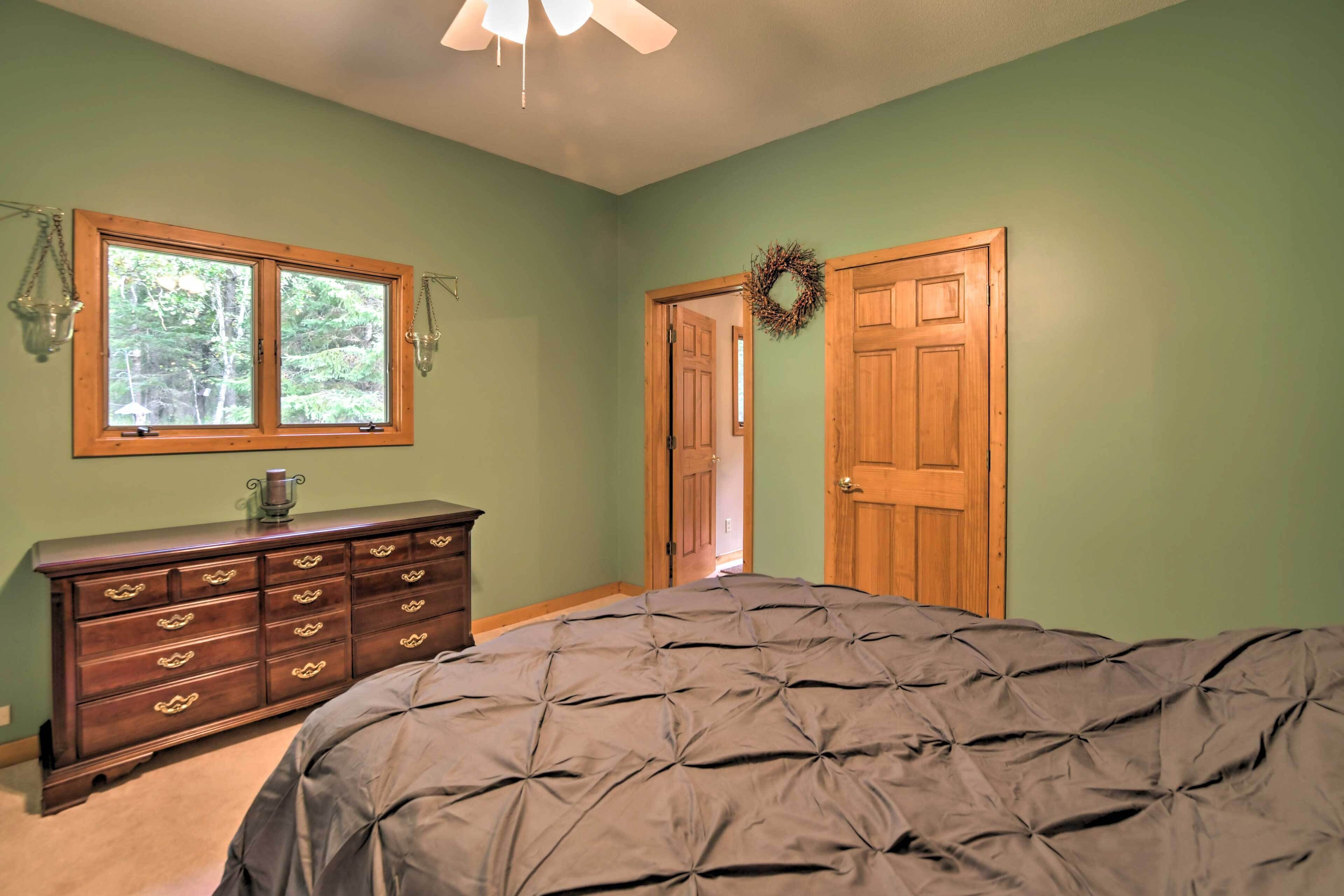 A bedroom with a large bed, a dresser, a window, and a door.
