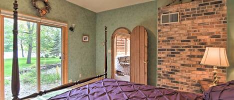 A bedroom with a large bed, a brick wall, a ceiling fan, a window, and a door leading to another room.