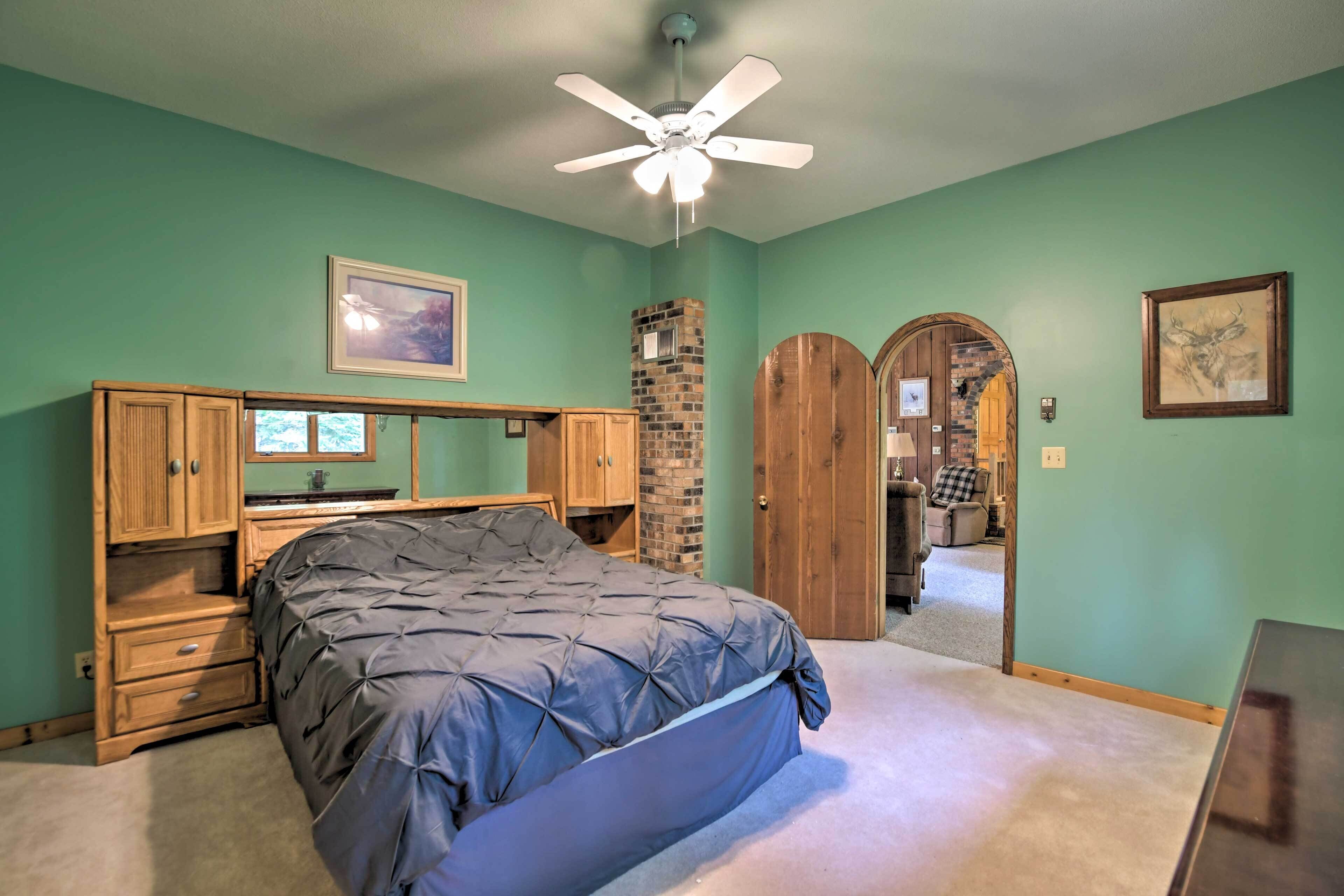 A bedroom with a bed, wooden cabinets, a brick fireplace, and a ceiling fan.