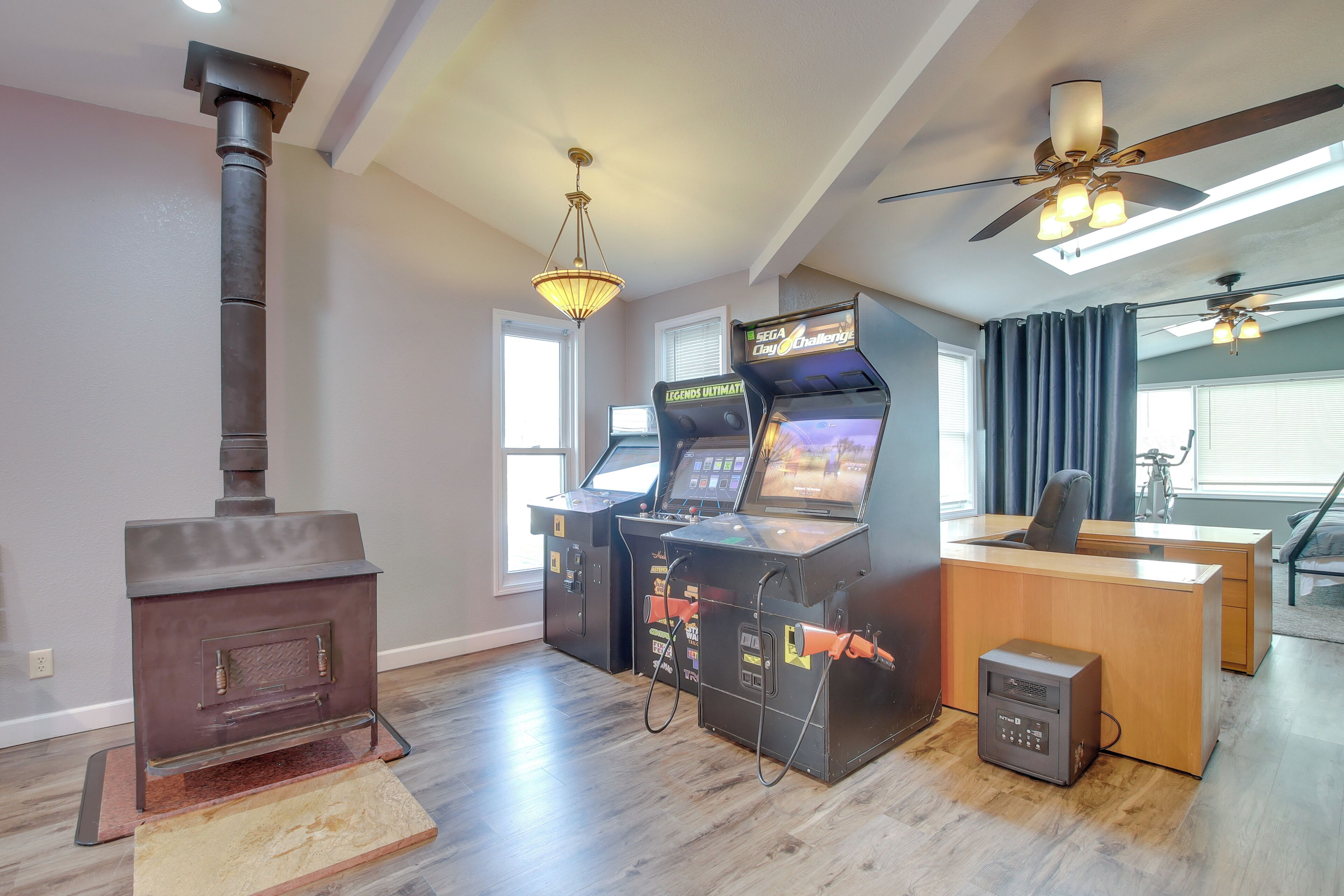 Een kamer met een houtkachel, gameconsoles en een bureau.
