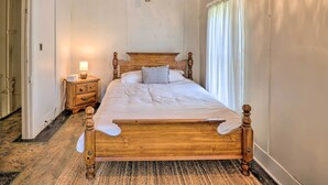 Ein Schlafzimmer mit einem hölzernen Bett, einem Nachttisch mit Lampe und einem Fenster mit Vorhängen.