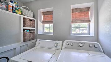 A laundry room with two washing machines, wicker baskets, and a shelf with cleaning supplies.