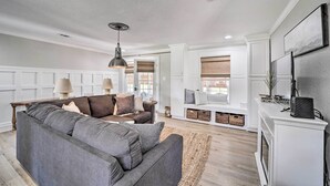 Un salon moderne avec un canapé d’angle, une cheminée et une grande fenêtre équipée de stores.