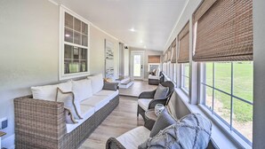 Une véranda aménagée avec des meubles en osier, de grandes fenêtres et une vue sur l’extérieur.