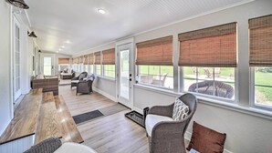 Un patio couvert comprenant une longue table en bois, des meubles en osier et de grandes fenêtres équipées de stores.
